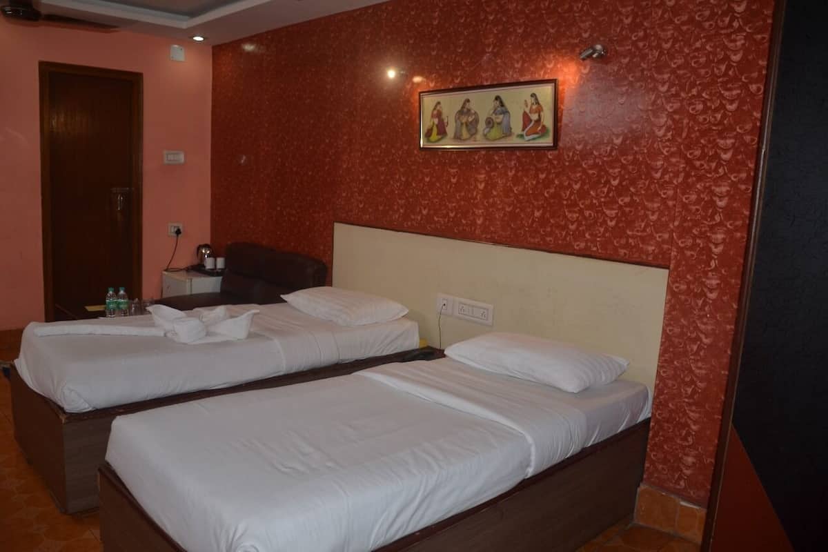 A hotel room with two single beds, a wooden headboard, a wall-mounted painting, and a small table with a lamp and a bottle.