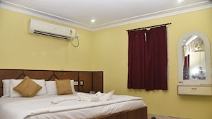 A hotel room with a large bed, a mounted air conditioner, a mirror, and a curtain. - Hotel Ispat International (Asansol)