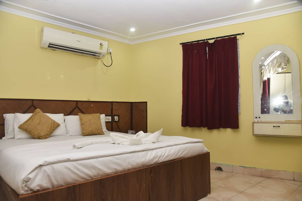 A hotel room with a large bed, a mounted air conditioner, a mirror, and a curtain.