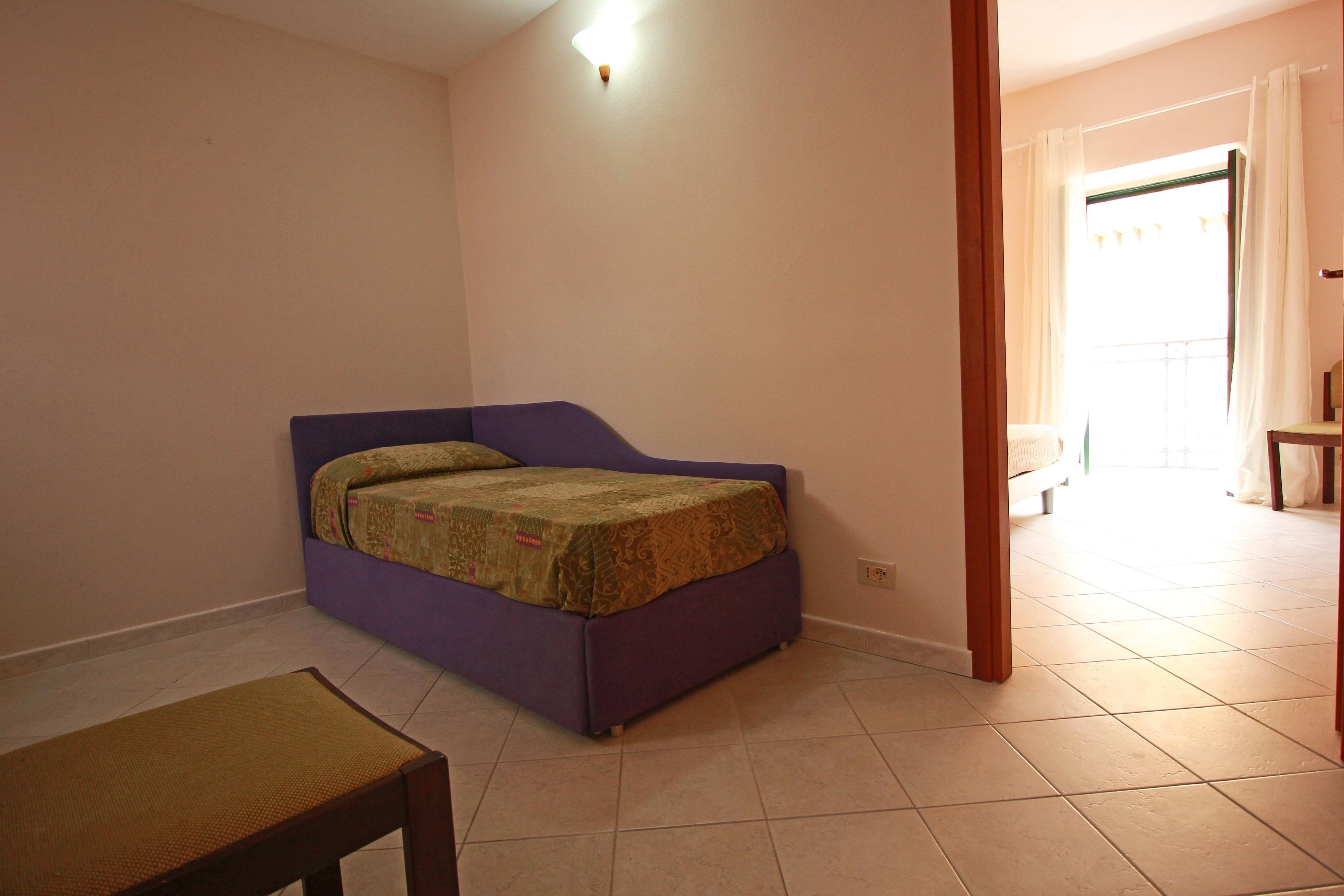 Une chambre avec un lit violet, une petite table et une chaise.