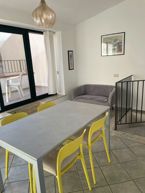 Un comedor con mesa y sillas, un sofá, una barandilla y un ventanal con cortinas.