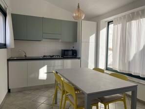 Cocina compacta con comedor, que incluye estufa a gas, microondas y ventana con cortinas.