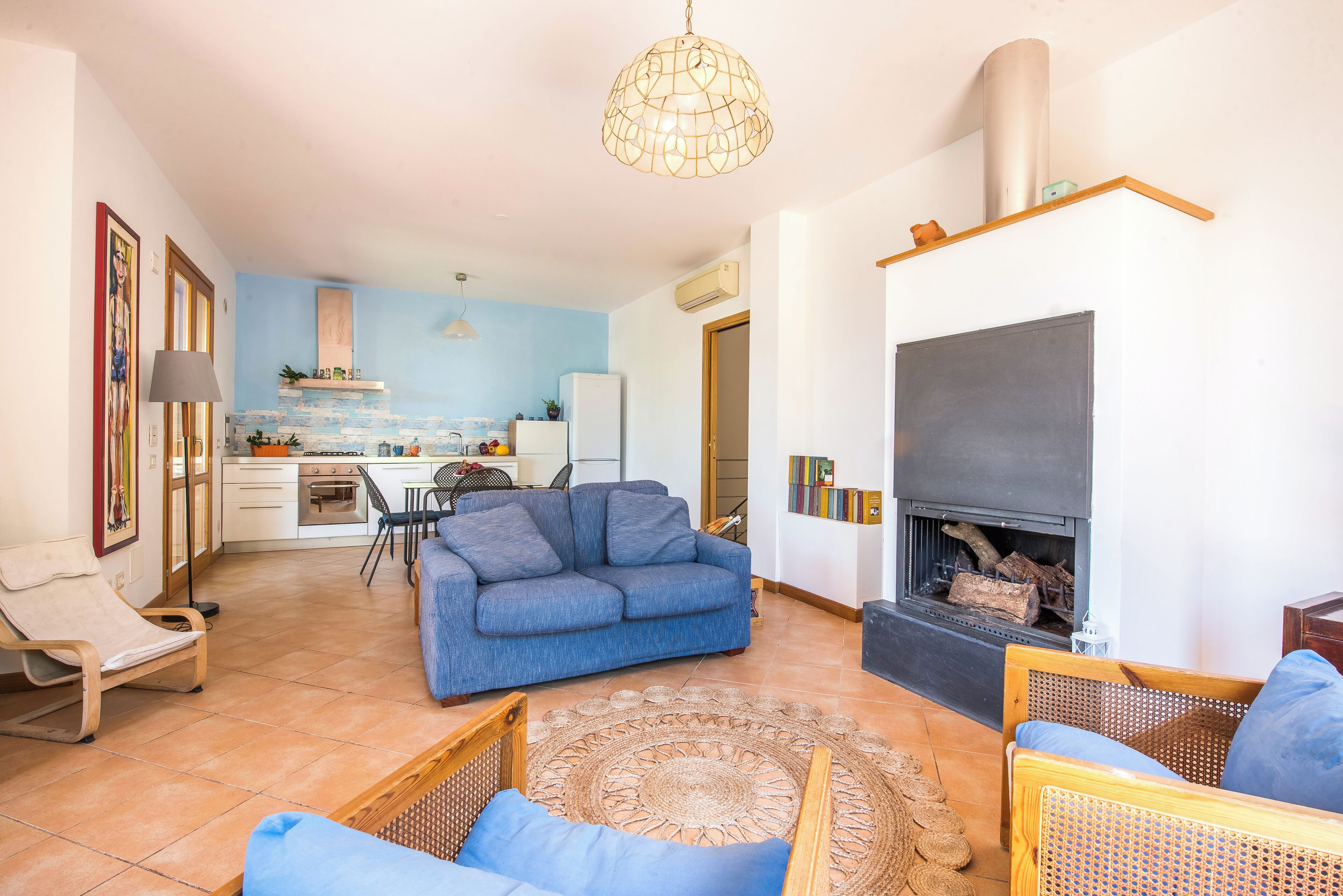 A living room with a sofa, chairs, a fireplace, and a kitchen in the background.
