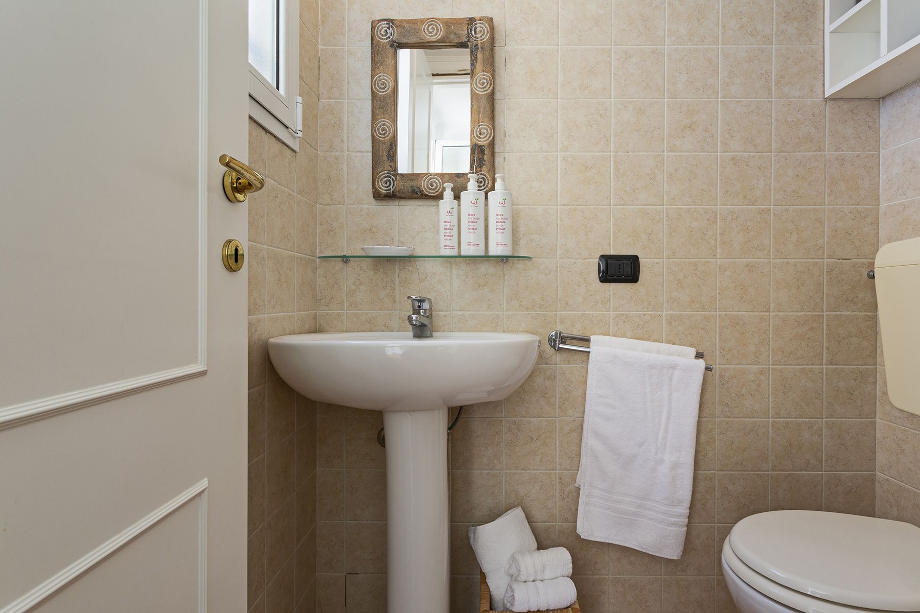 Ein Badezimmer mit einem weißen Waschbecken, einer Glasablage für Pflegeartikel, einem Handtuchhalter und einer Toilette.