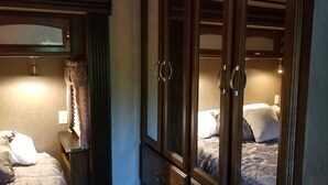 Ein Hotelzimmer mit großem Kleiderschrank, einem Bett mit gemustertem Überwurf und einem Nachttisch mit Lampe.