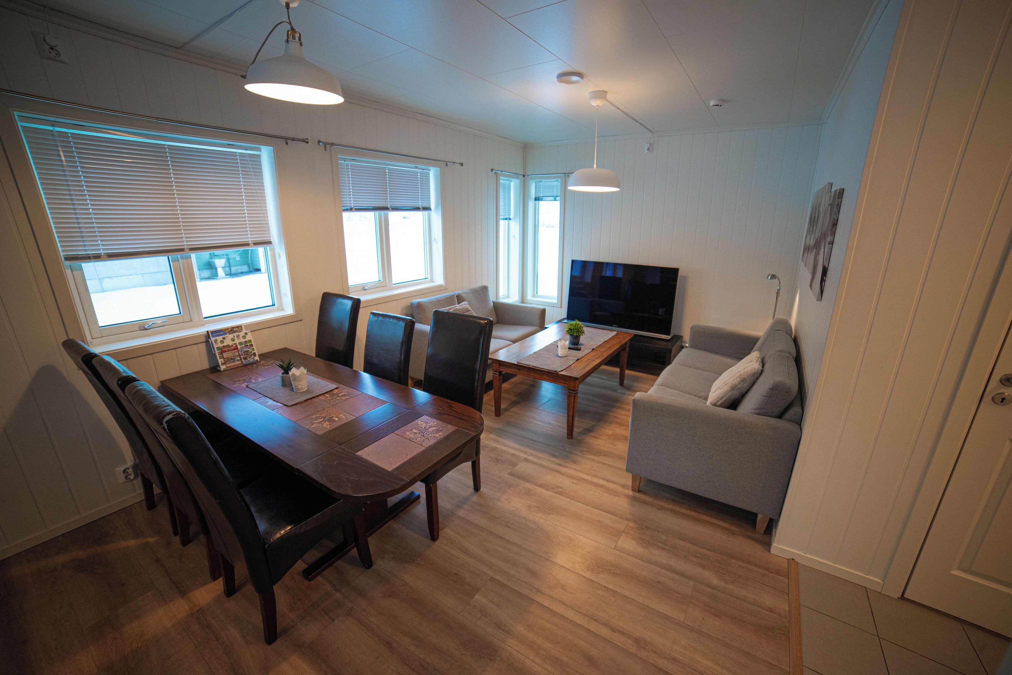 A modern living room with a wooden dining table, a grey sofa, and a TV.