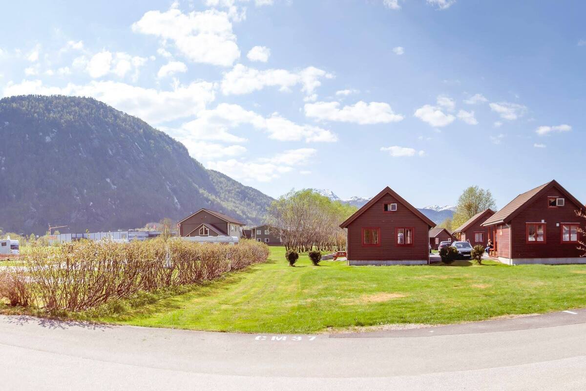 Eine Reihe roter Holzhütten vor einer Bergkulisse, mit blauem Himmel und einem gepflegten Rasen.