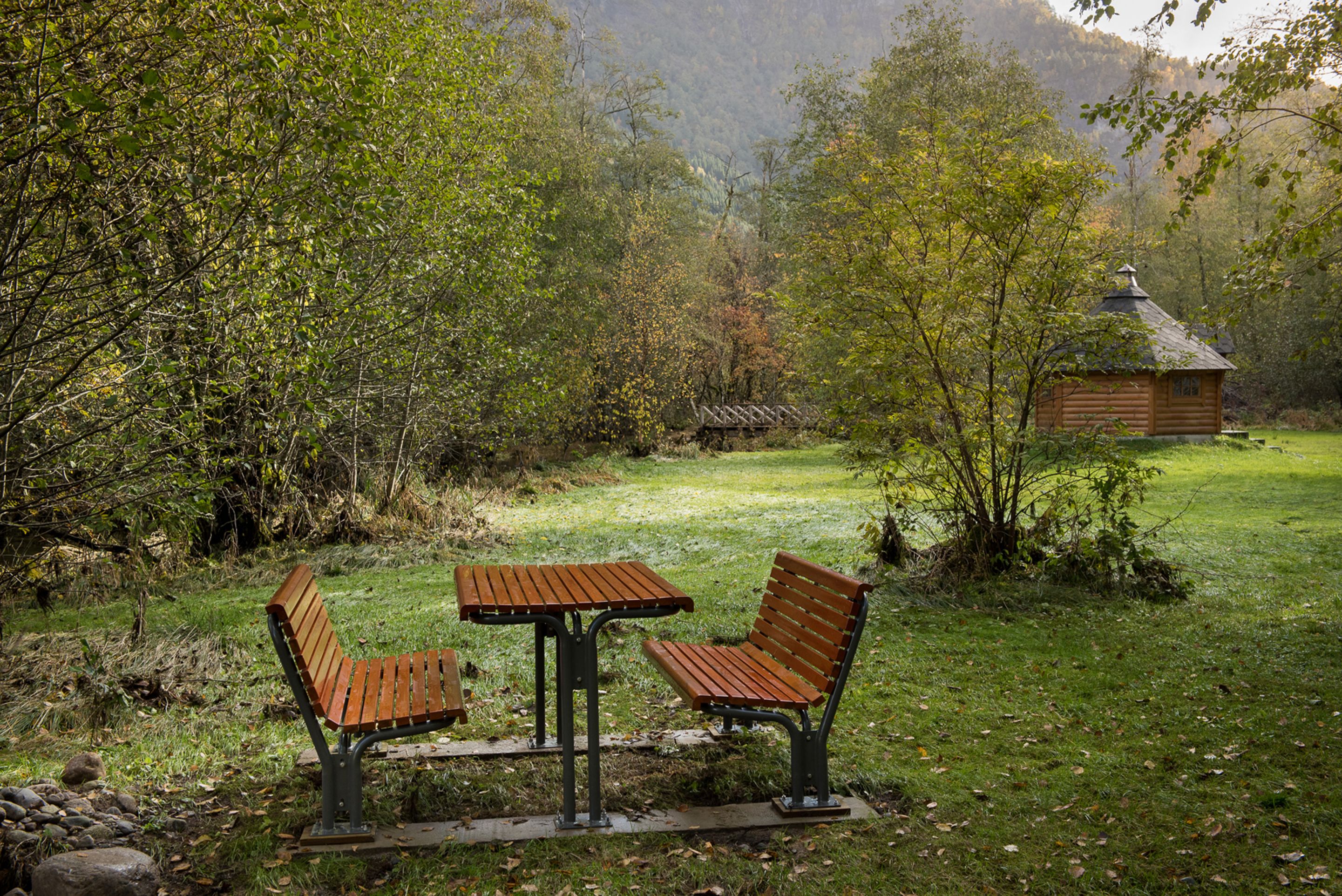 A wooden bench and table in a grassy area with a cabin in the background.