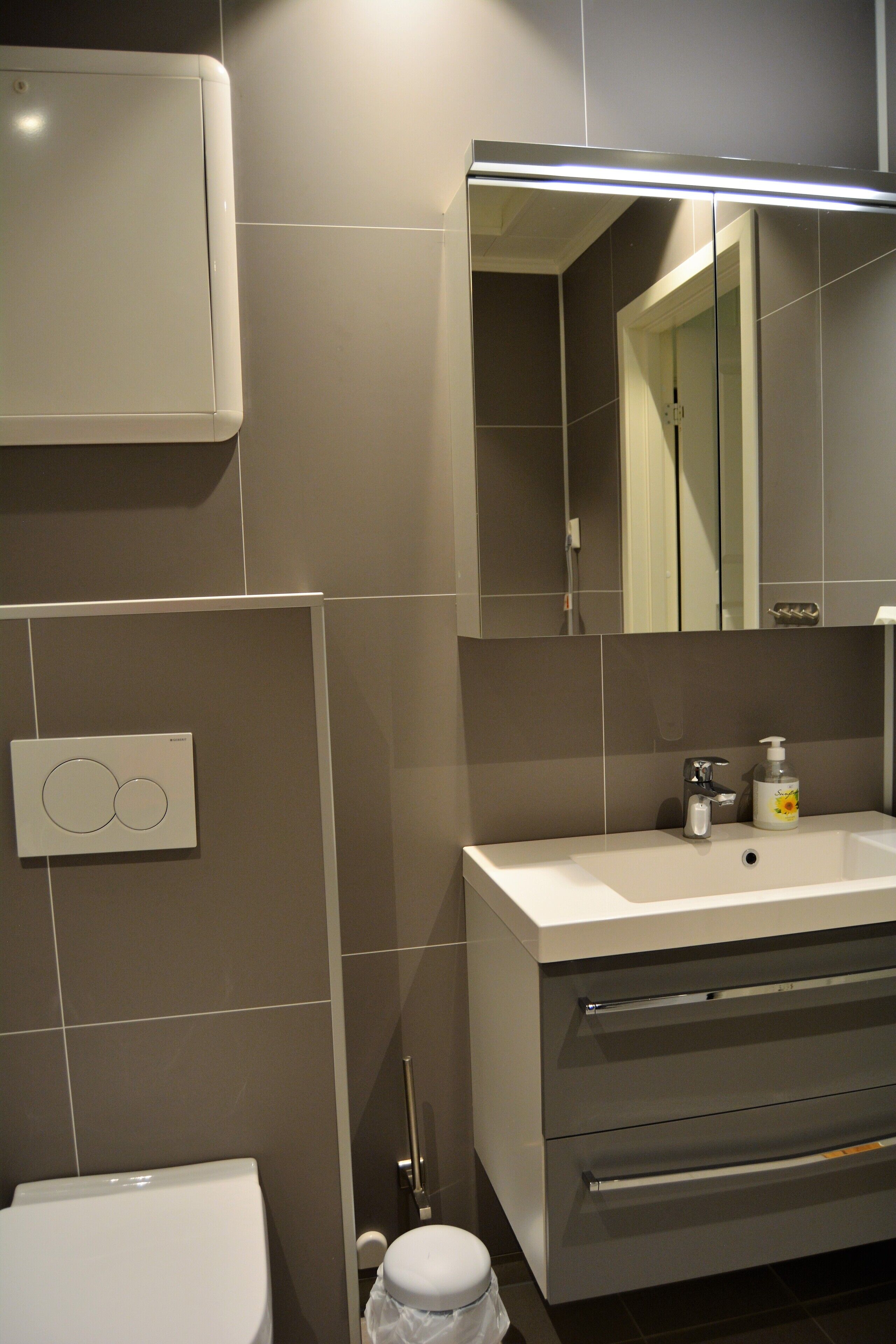 Un baño moderno con inodoro, lavamanos con espejo y zona de ducha.