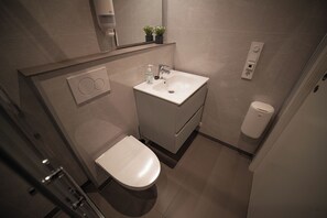 A modern bathroom with a white sink, toilet, and shower. There are two small potted plants on the wall above the sink. - Førde Gjestehus og Camping (Sunnfjord)