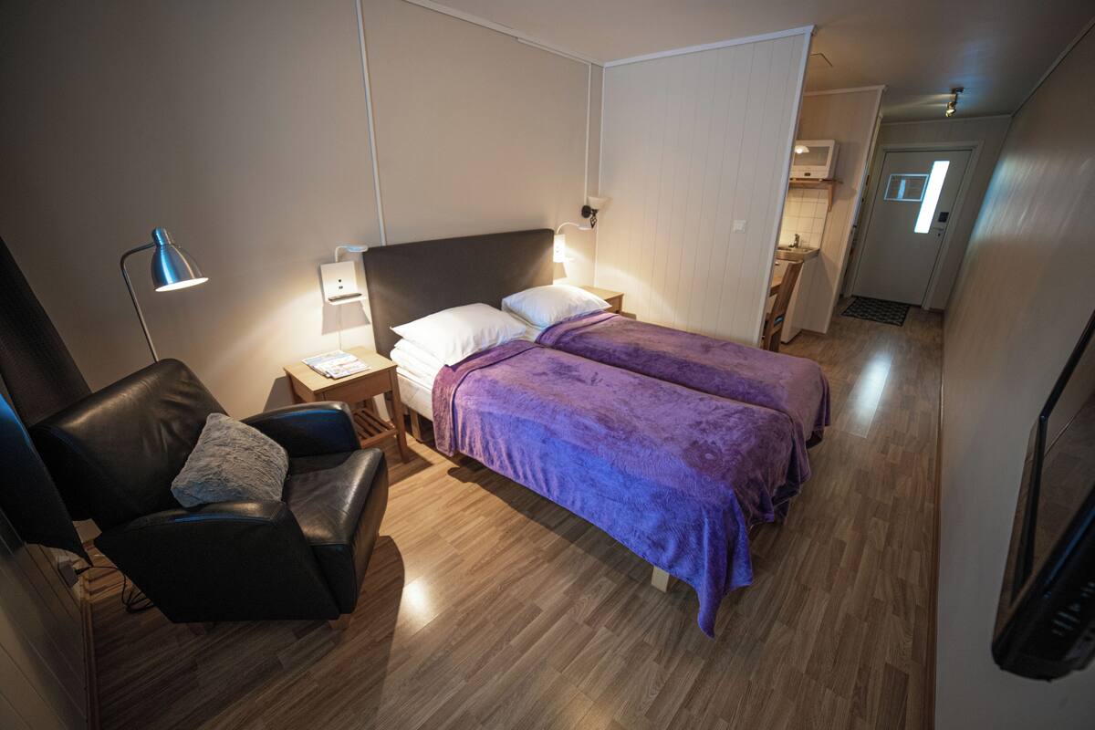 Ein Schlafzimmer mit zwei Betten, einem Sessel, einem Schreibtisch und einer Lampe.