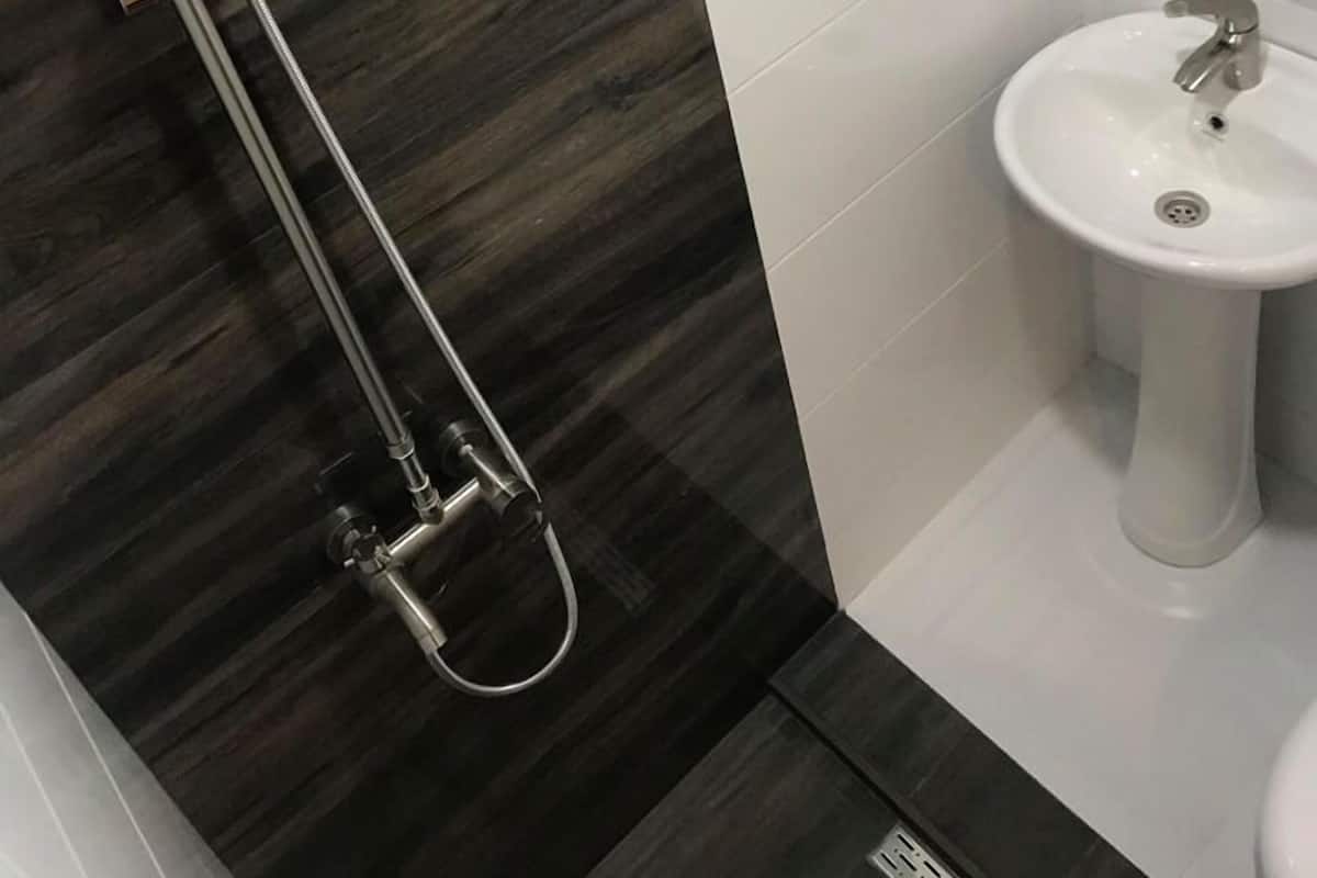 A modern bathroom with a dark wood vanity, a white sink, and a shower with a handheld showerhead.