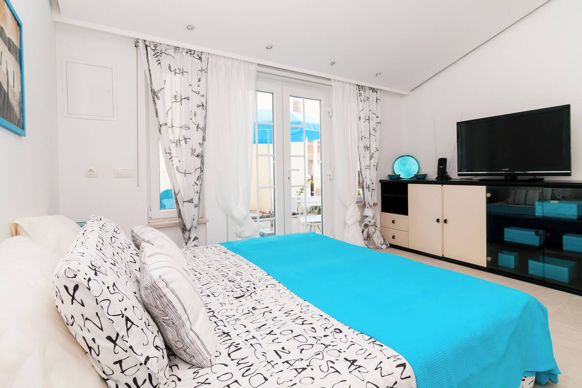 Une chambre à coucher avec un lit, une télévision, une armoire et un balcon agrémenté de parasols bleus.
