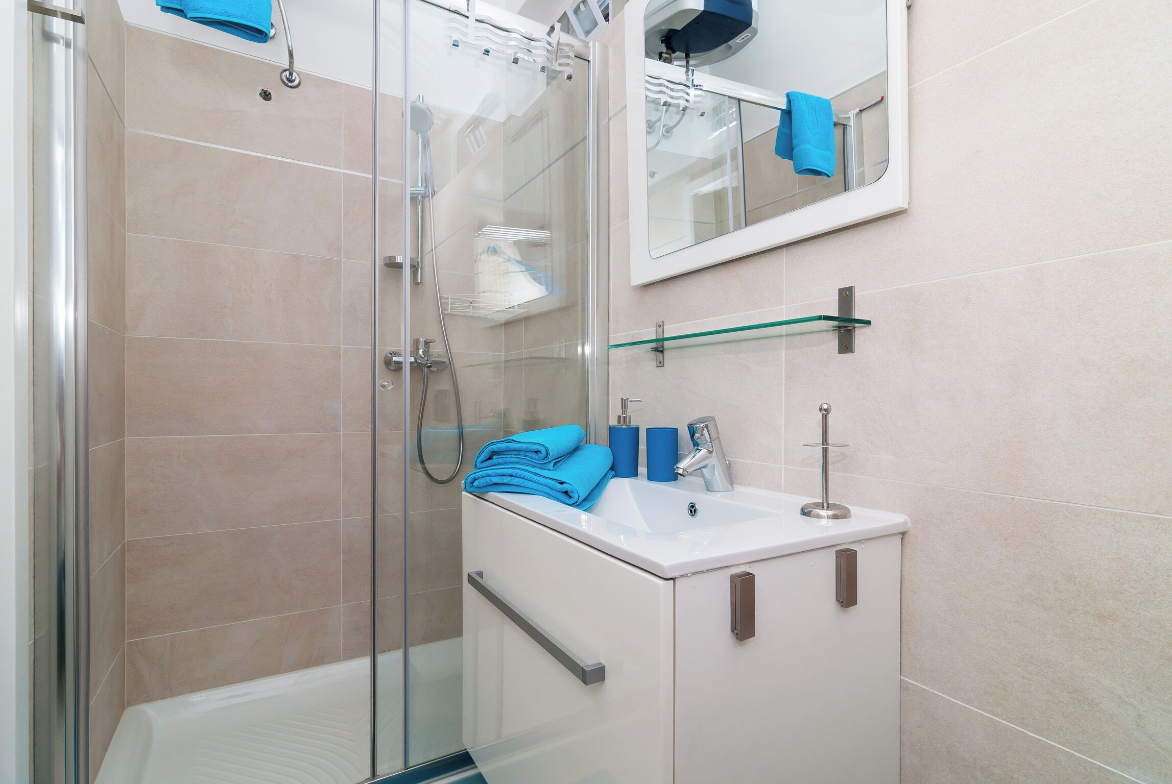 A modern bathroom with a glass shower enclosure, a white sink with a blue towel, and a mirror above the sink.