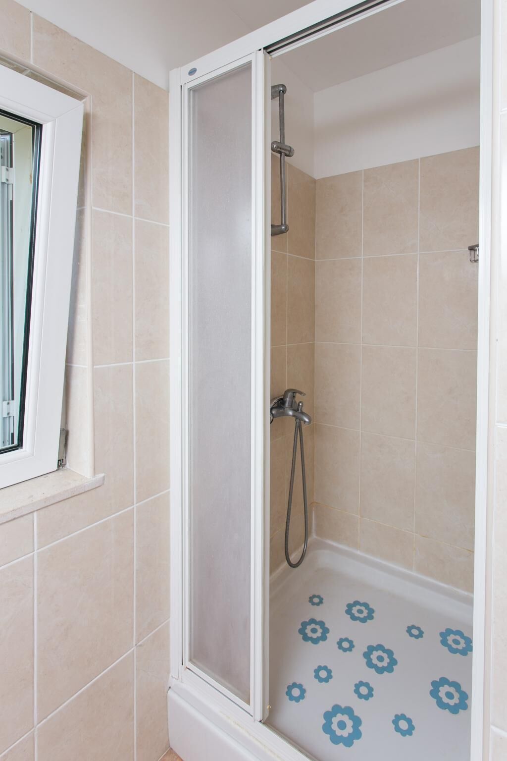 Una ducha con puerta de cristal, azulejos color beige y un estampado floral azul en el suelo.