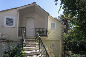 A two-story building with a front door, a small balcony with a metal railing, and a staircase leading to the entrance.
