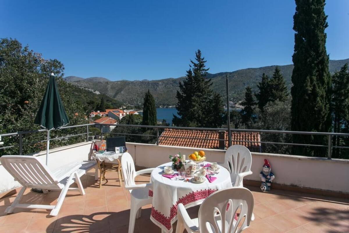A terrace with a table set for dining, overlooking a scenic landscape with mountains and a body of water.