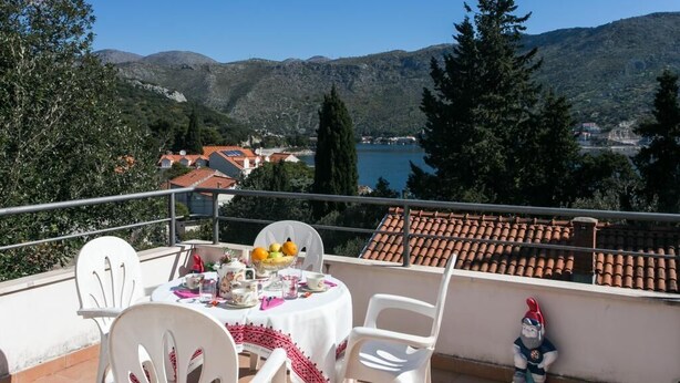 Eine Terrasse mit Esstisch, mit Blick auf eine Berglandschaft und ein Gewässer.