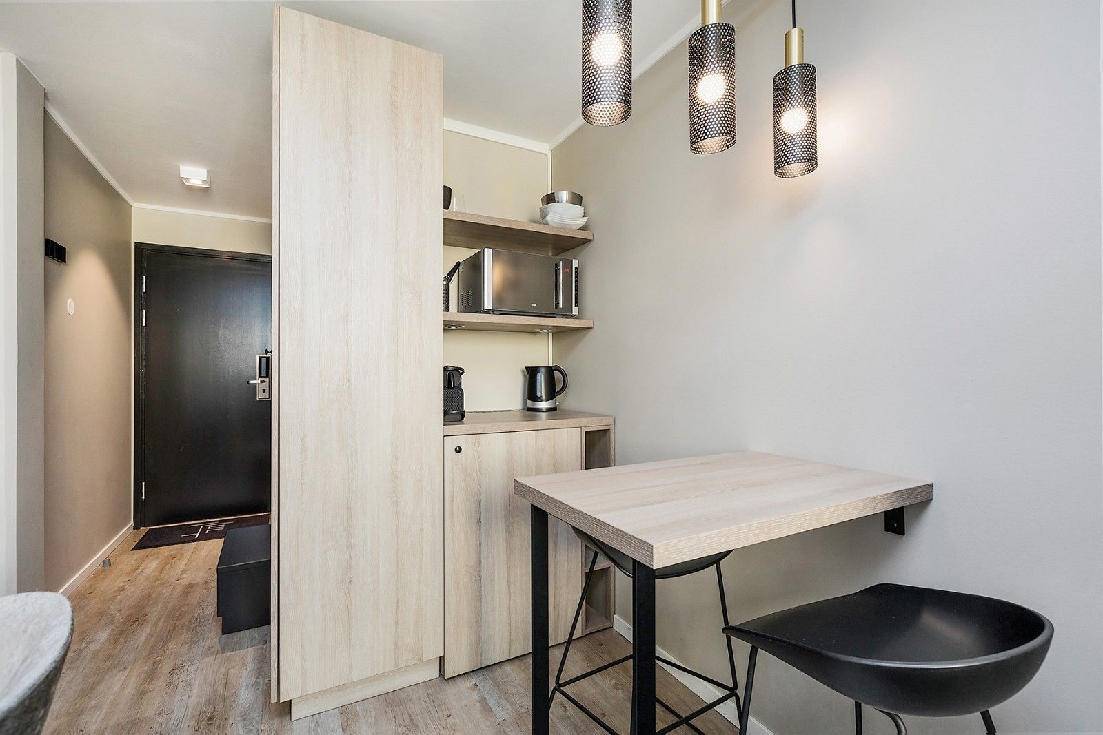 Une cuisine moderne avec un plan de travail en bois, un évier noir et un tabouret noir. Trois suspensions sont suspendues au-dessus du plan de travail.