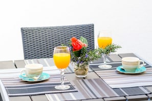 A table set with two cups, two glasses of orange juice, and a vase with a red rose and greenery.
