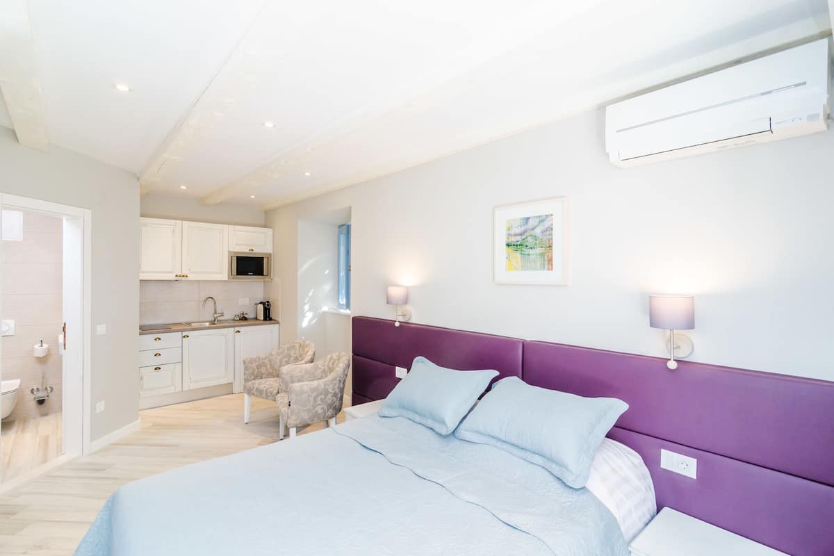 Ein modernes Schlafzimmer mit einem Bett, einem violetten Kopfteil, zwei Nachttischlampen und einer Wand-Klimaanlage.