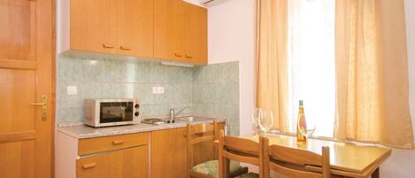 A compact kitchen with wooden cabinets, a microwave, a sink, and a dining table with chairs.