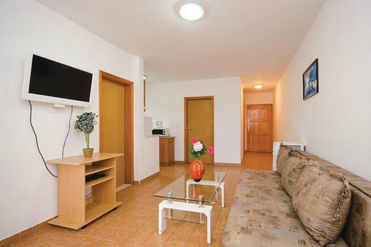 Uma sala de estar com televisão, cafeteira, sofá e uma pequena mesa com um vaso de flores.