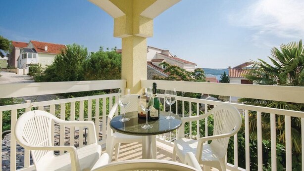 A balcony with a round table and two white chairs, overlooking a coastal area with houses and greenery. - Apartments Ciovo (Okrug)