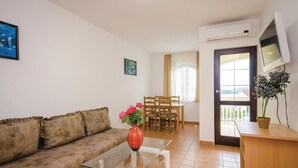 A living room with a sofa, a glass coffee table, a dining area with a table and chairs, a potted plant, and a TV mounted on the wall. - Apartments Ciovo (Okrug)