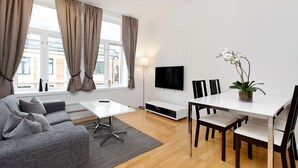 Un salon moderne avec un canapé gris, une table basse blanche, un téléviseur et un coin repas comprenant une table et des chaises blanches.