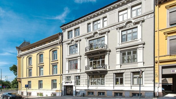 Un immeuble à plusieurs étages, de style architectural classique, doté de grandes fenêtres et d’un balcon central.