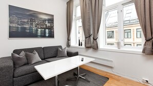Un salon moderne avec un canapé gris, une table basse blanche et un tableau représentant un paysage urbain accroché au mur.