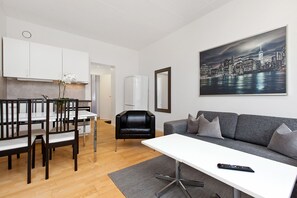 A modern living room with a white sofa, a dining table with chairs, a black leather chair, and a remote control on the table.