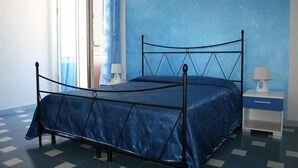 Una cama individual con estructura metálica y colcha azul en habitación con paredes azules y piso a cuadros.