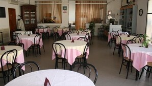 Un área de comedor con mesas redondas cubiertas con manteles rosa y blancos, rodeada de sillas negras.