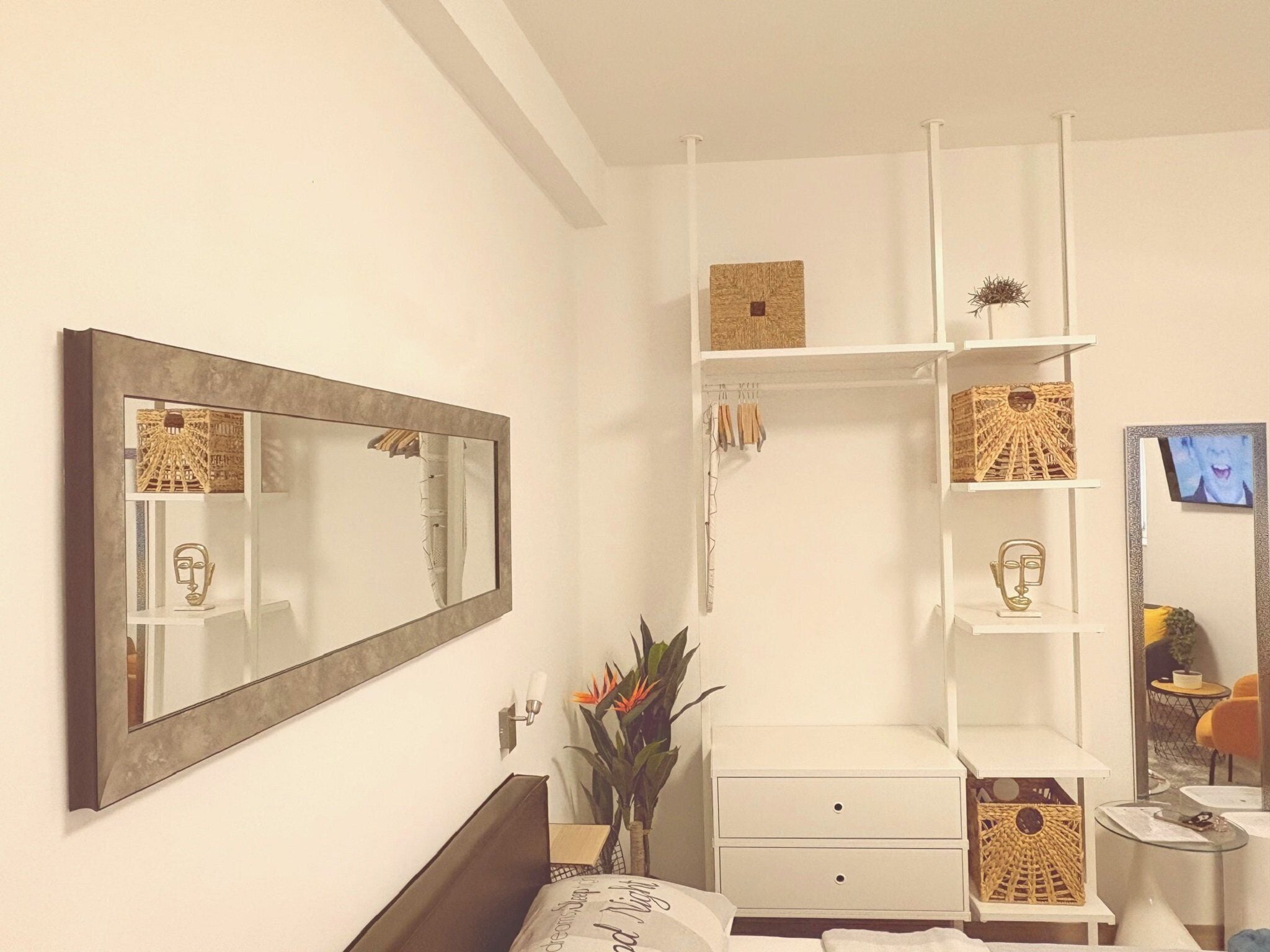 A modern bedroom with a large mirror, a bedside table, a wardrobe, and a small seating area with a chair and table.