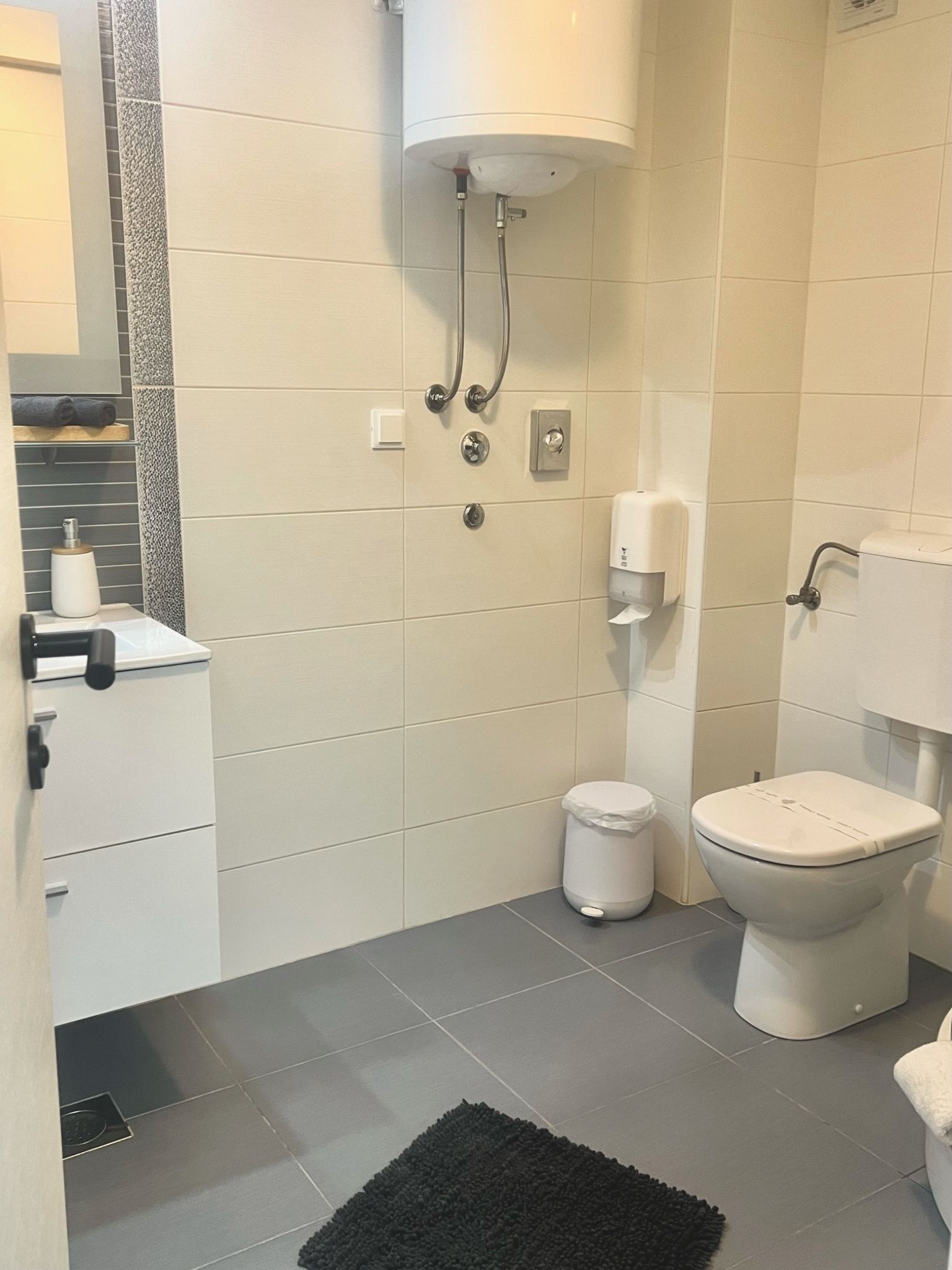 A bathroom with a toilet, a sink, a shower, and a hand dryer.