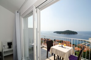 A balcony with a table set for two, overlooking a coastal view with a small island and a marina.