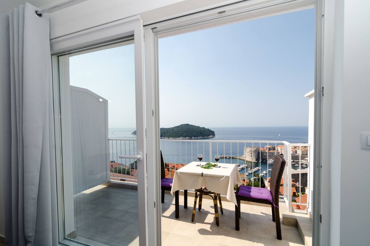 A balcony with a table and chairs, a view of the sea, and a distant island.