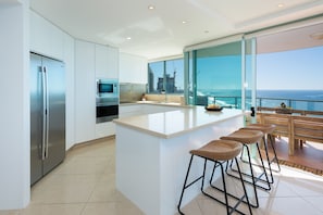 A modern kitchen with a large island, bar stools, and a view of the ocean.