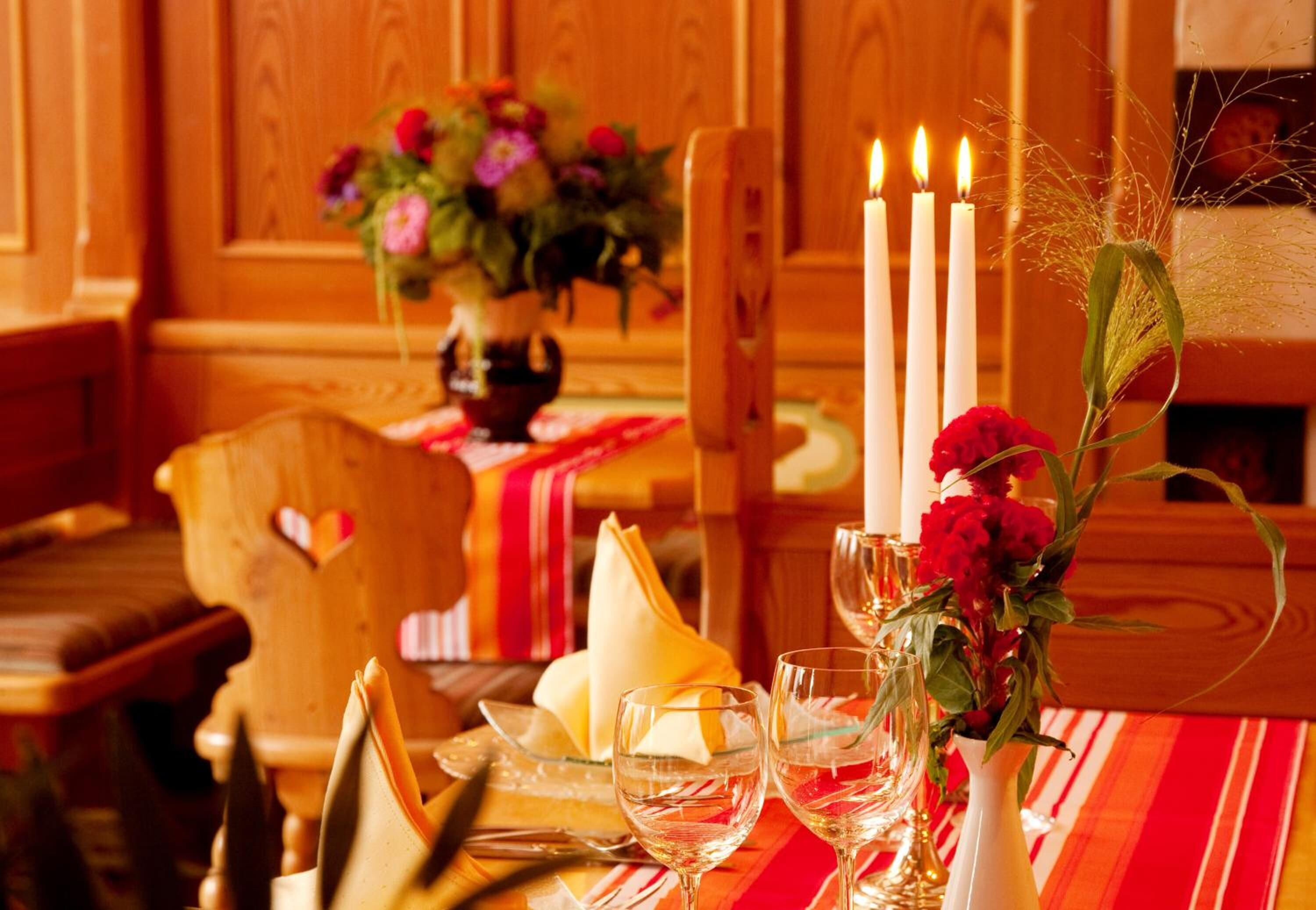 A dining table with candles, a vase of flowers, and a heart-shaped cushion on a wooden chair.