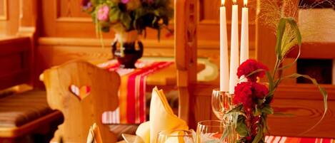 A dining table with candles, a vase of flowers, and a heart-shaped cushion on a wooden chair.