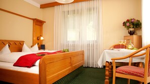 Ein Hotelzimmer mit einem hölzernen Bett, einem kleinen Tisch mit zwei Weingläsern und einer Vase mit Blumen.