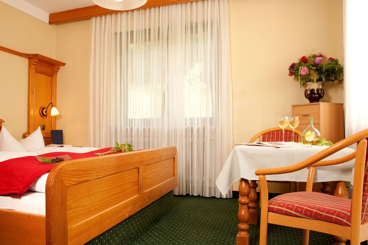 A hotel room with a wooden bed, a small table with two glasses of wine, and a vase with flowers.