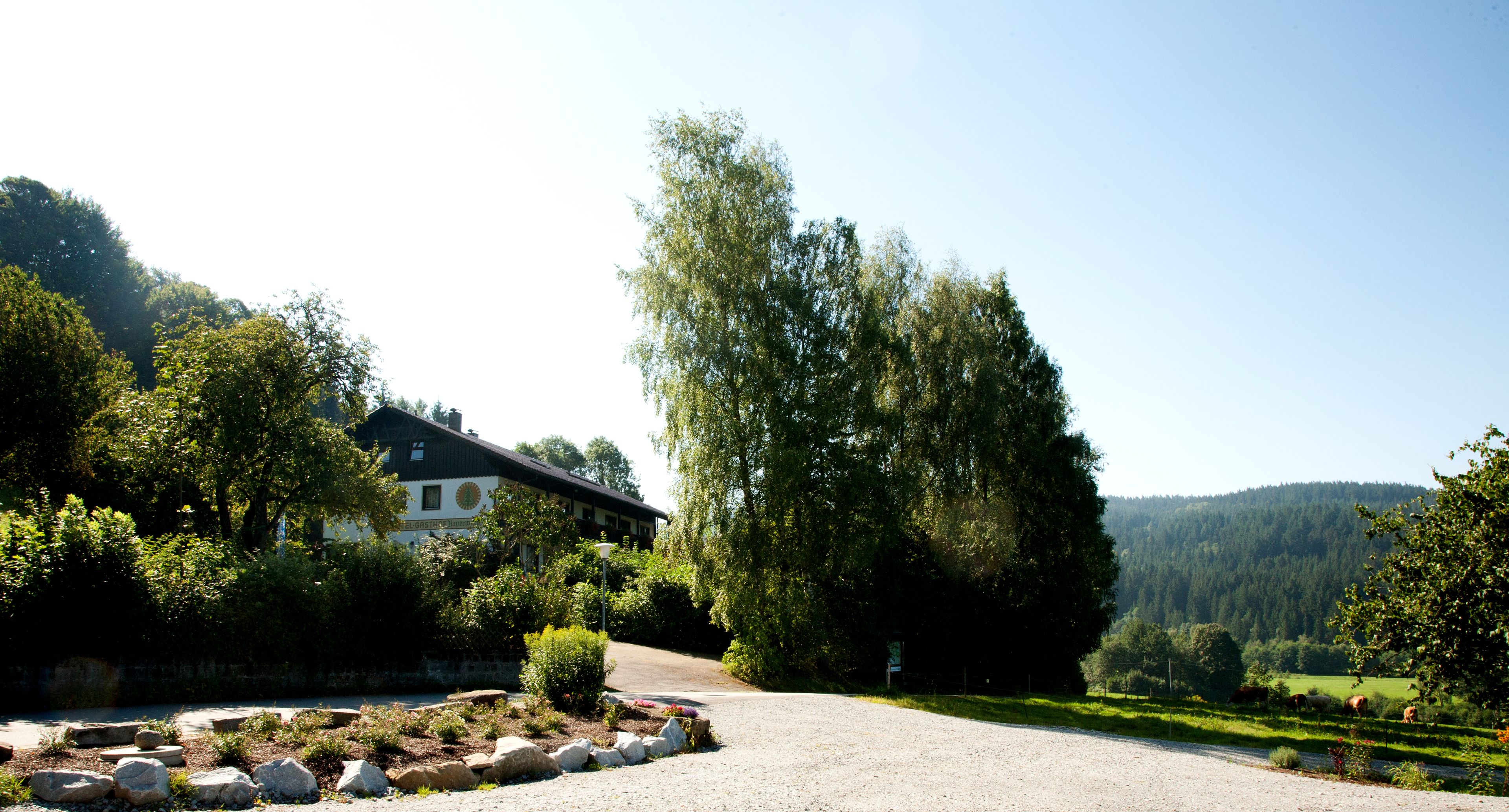 Un bâtiment doté d’un toit en pente, entouré d’une allée gravillonnée et d’un jardin aménagé avec des rochers et des arbustes.