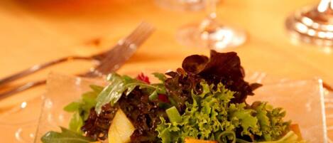 A glass plate with a salad on a table, accompanied by wine glasses and a teapot.