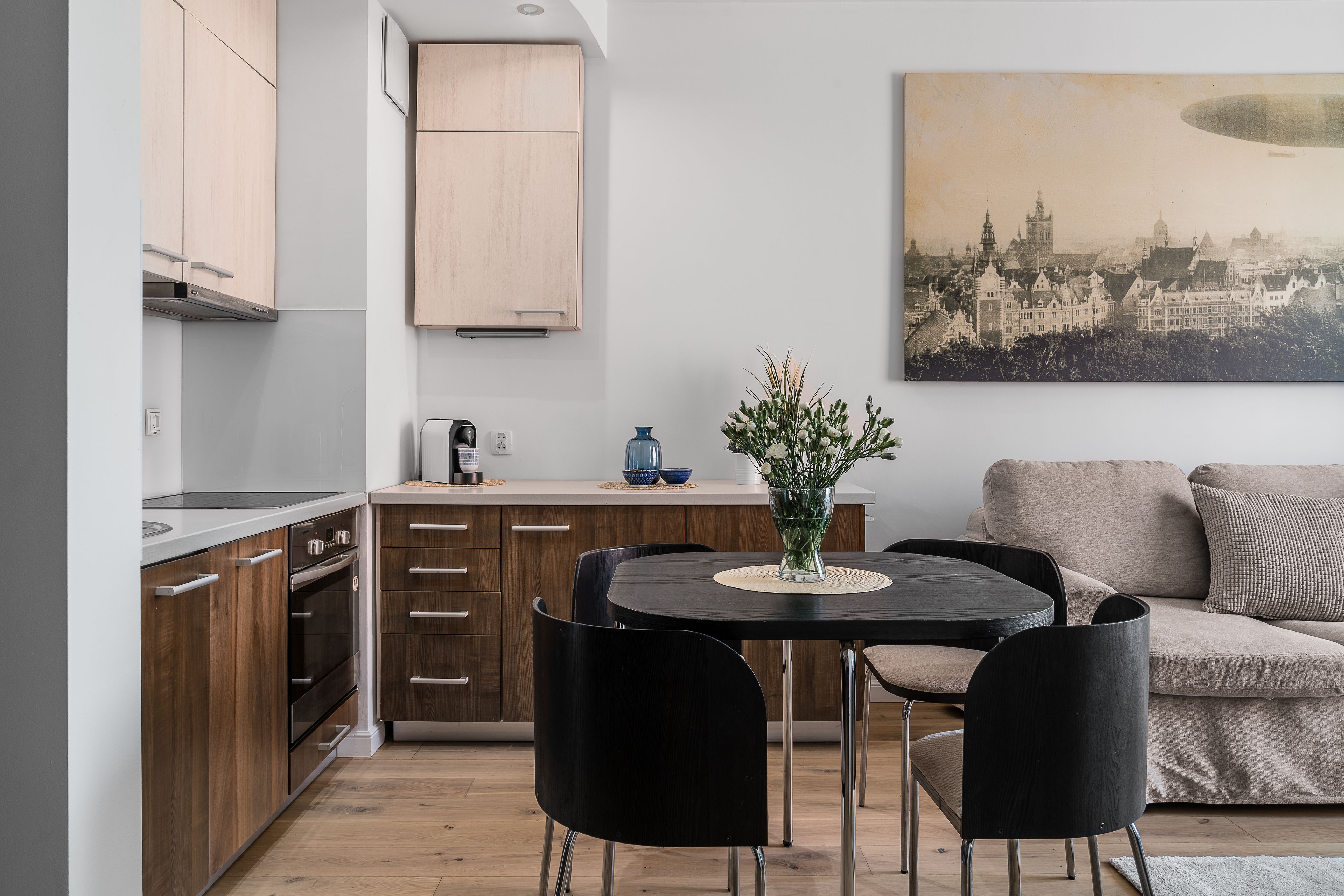 A modern kitchen with wooden cabinets, a dining table with two chairs, and a sofa in the living area.