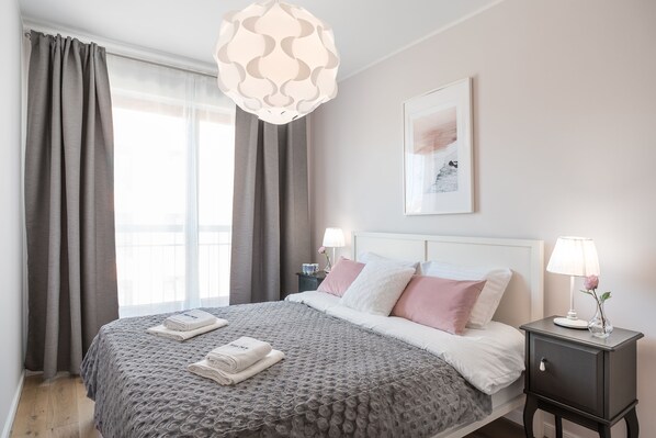 A neatly made bed with a patterned bedspread, a bedside table with a lamp and a vase, and a framed picture on the wall.