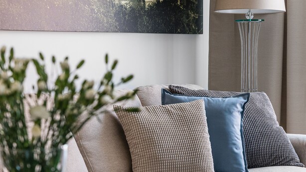 Ein modernes Wohnzimmer mit einer Couch, dekorativen Kissen, einer Pflanzvase und einem Stadtbild an der Wand.