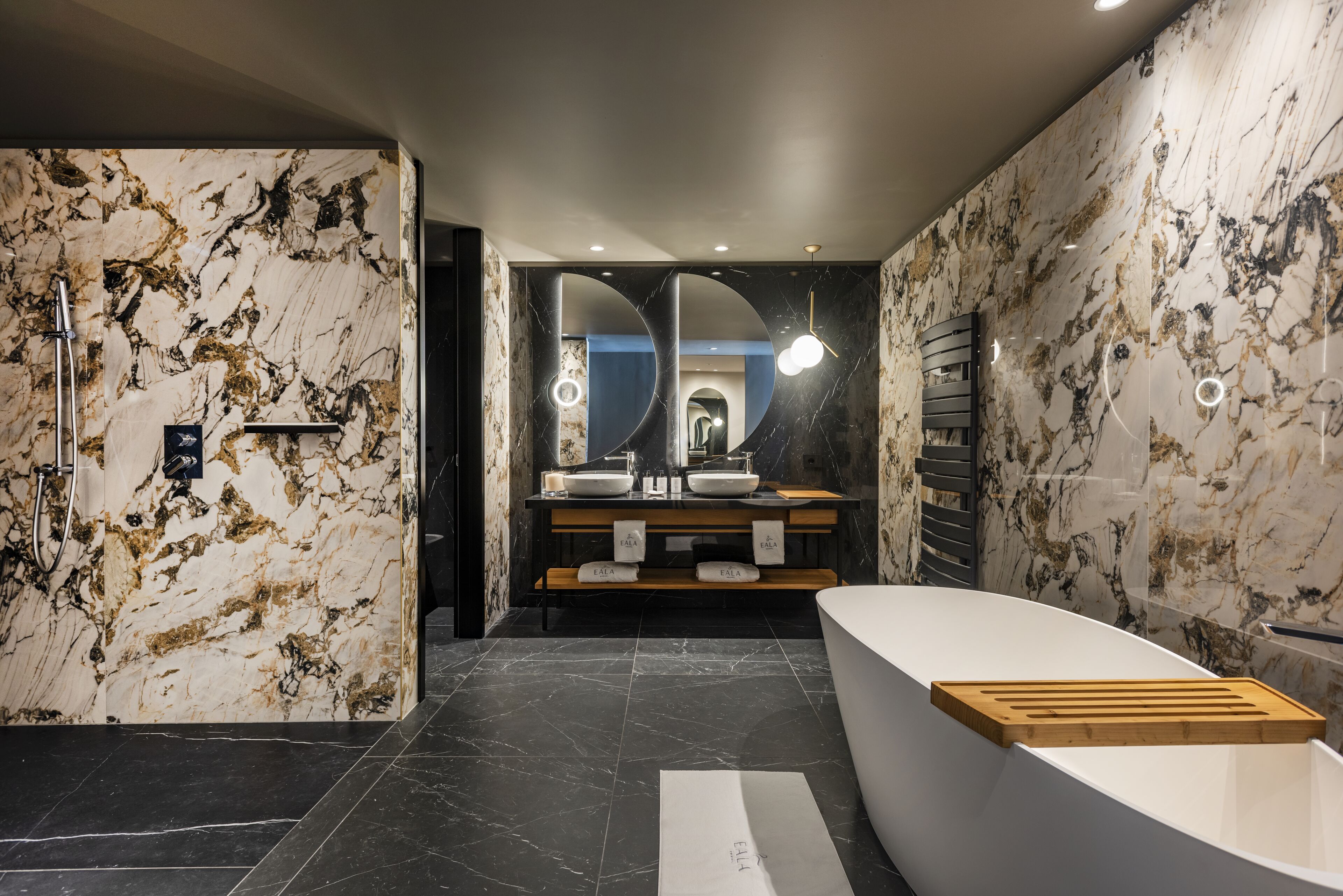 A modern bathroom with marble walls, a freestanding bathtub, and a double sink vanity.